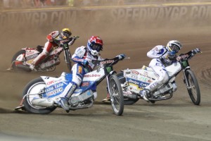 Nicki Pedersen (červená) bojuje s Peterem Kildemandem (bílá) před zraky Macieje Janowskeho